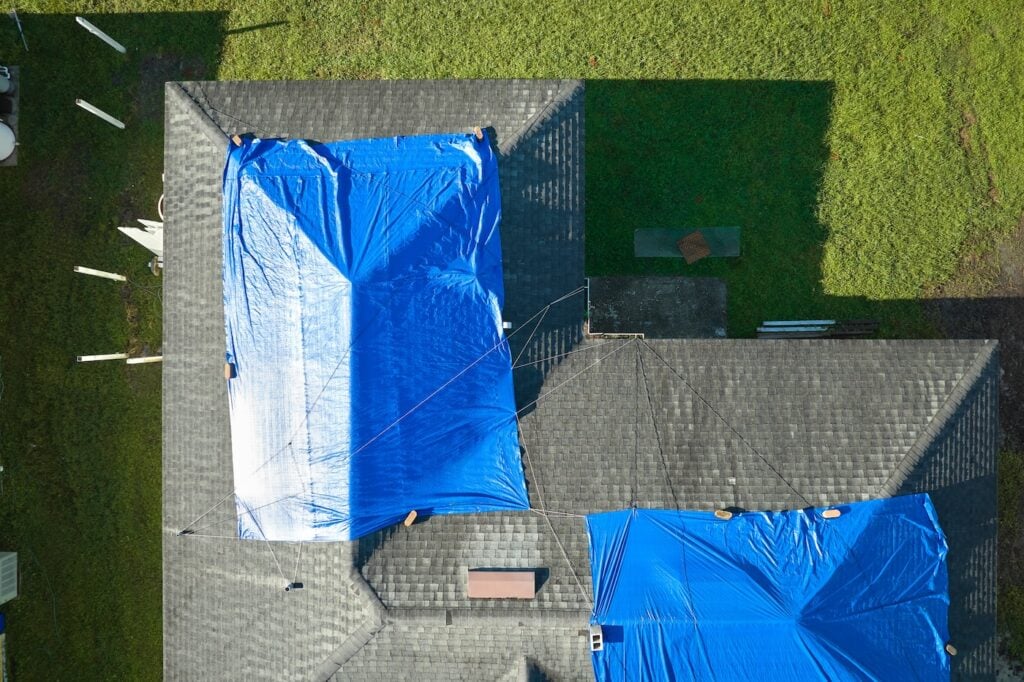 Top view of leaking house roof covered with protective tarp sheets against rain water leaks until replacement of asphalt shingles. Damage of building rooftop as aftermath of hurricane Ian in Florida