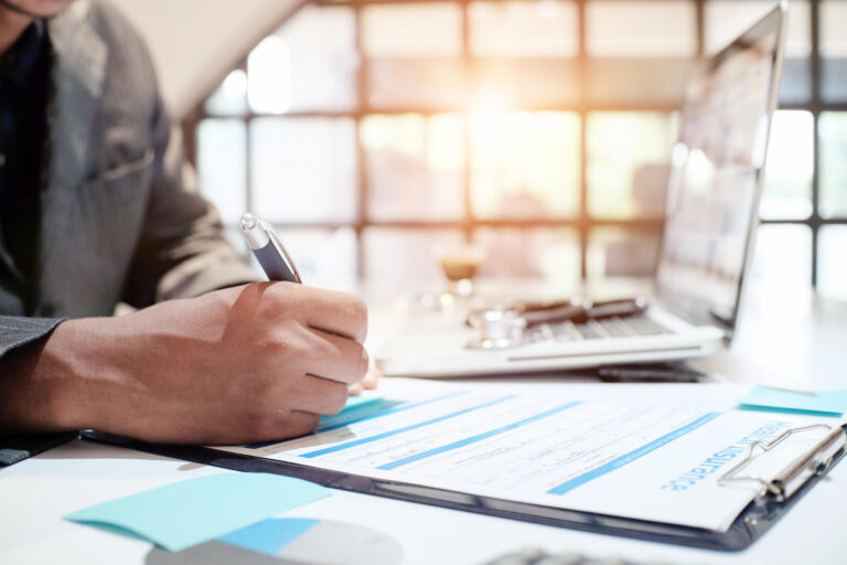how to get insurance to pay for roof replacement-insurance adjuster writing on a document next to a laptop