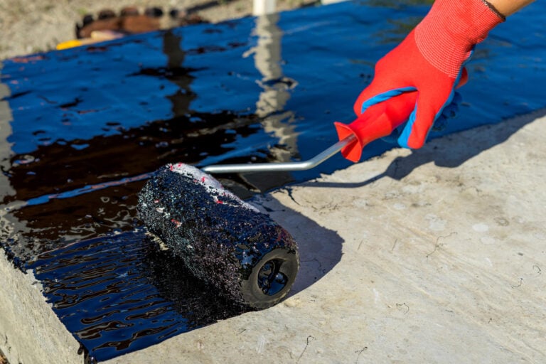 rubber roof coating-close up of a person applying rubber coating to a commercial roof with a hand roller
