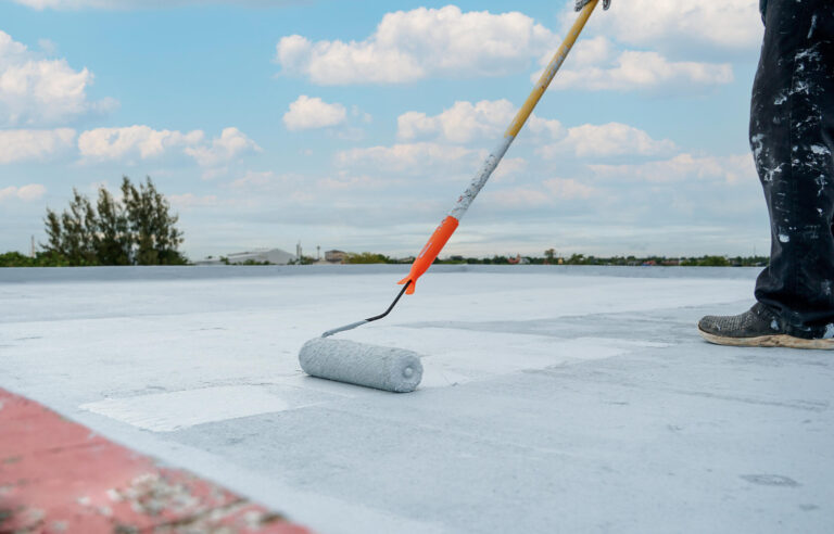 elastomeric roof coating-close up of roofer rolling on elastomeric roof coating to flat roof