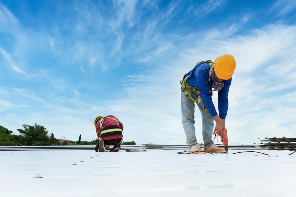 Two roofers installing metal roofing material to restore commercial building roof