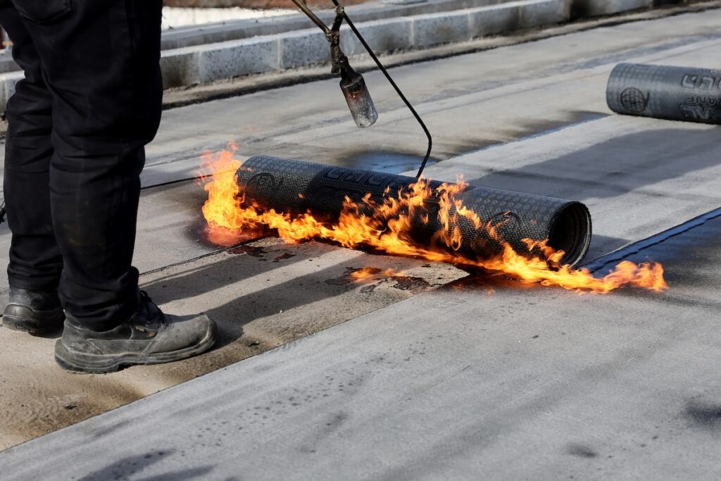 Professional construction workers using a blowtorch to glue modified bitumen roll sheet over a roof