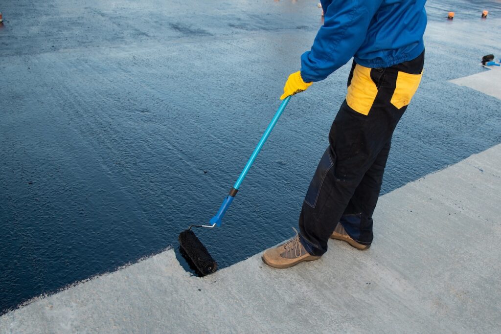 Waterproofing coating. Worker applies bitumen mastic on the foundation.