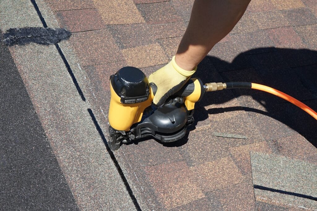  A roofer nailing shingles with air gun.