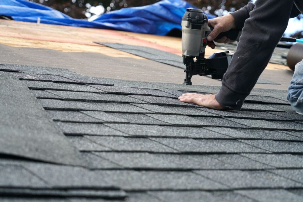 handyman using nail gun to install shingle to repair roof