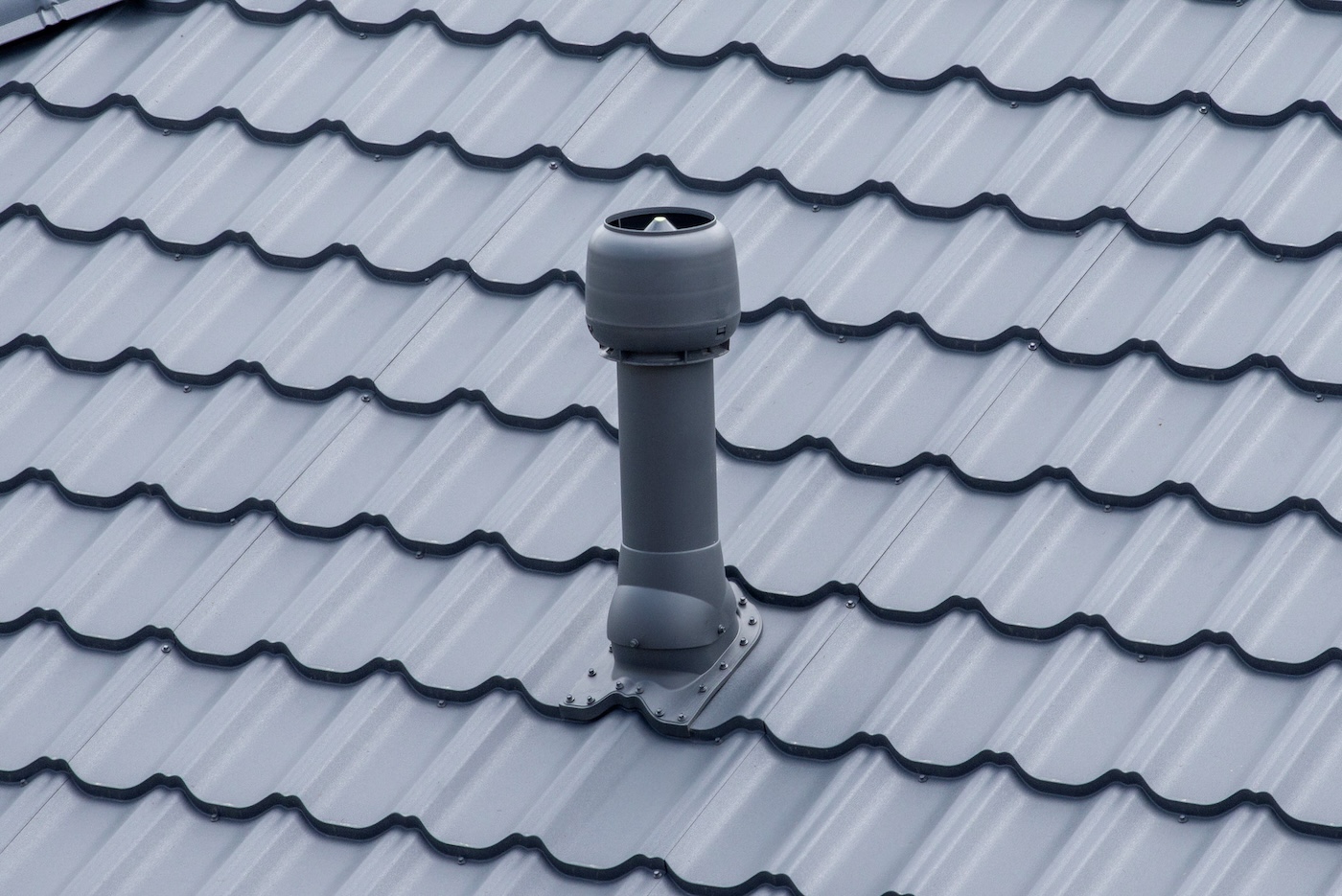 Plastic roof vent pipe on gray metal tile roofing