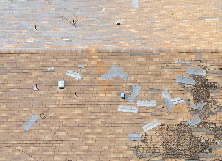 commercial roof wind uplift ratings Aerial view reveals a damaged roof. Shingles blown off during a storm and scattered. Structure requires urgent repair. Ideal for insurance or construction contexts