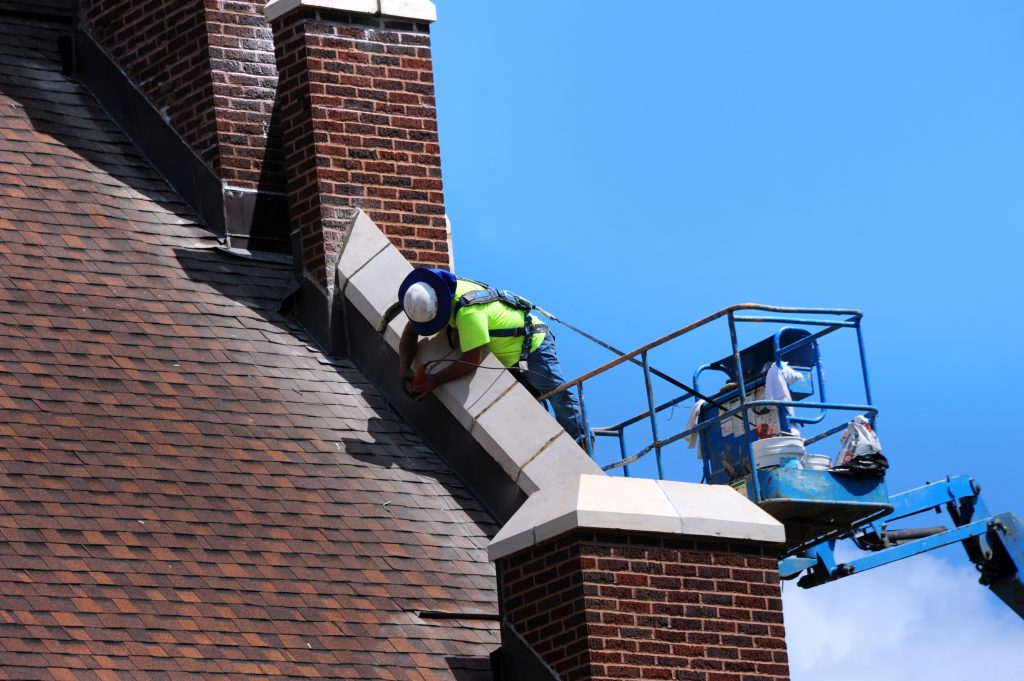 Construction worker uses sander in the repair of stonework on an historic church in Arkansas. He is standing on a lift and working on the roofline.